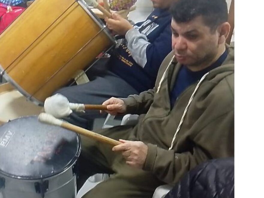 Participante da oficina de música tocando tambor com baquetas