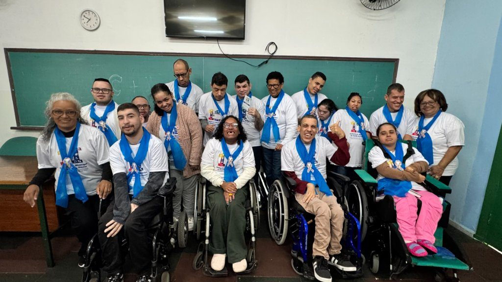 Grupo de pessoas atendidas pela AMME reunidas em sala, com lenços azuis, sorrindo